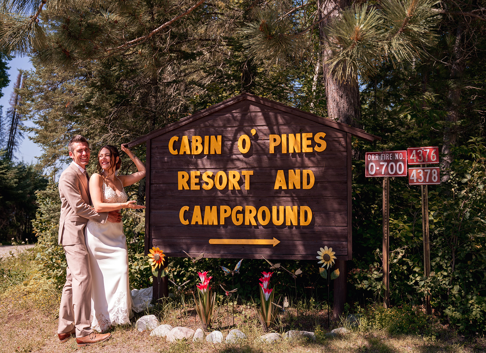 Bride and Groom in their wedding attire by Cabin O Pines sign in Northern Minnesota
